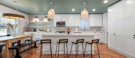 A modern kitchen with white cabinets, a central island with bar stools, and a green ceiling.