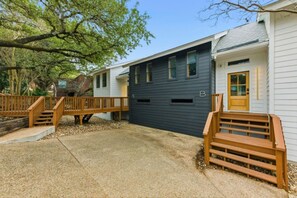 A two-story house with a dark blue garage, wooden stairs, and a small deck. - Austin Hideaway | 3BR Home with Private Backyard (Austin)