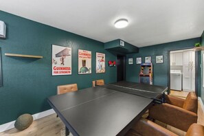Une pièce équipée d’une table de ping-pong, de chaises, d’une petite étagère et d’une porte donnant sur une buanderie.