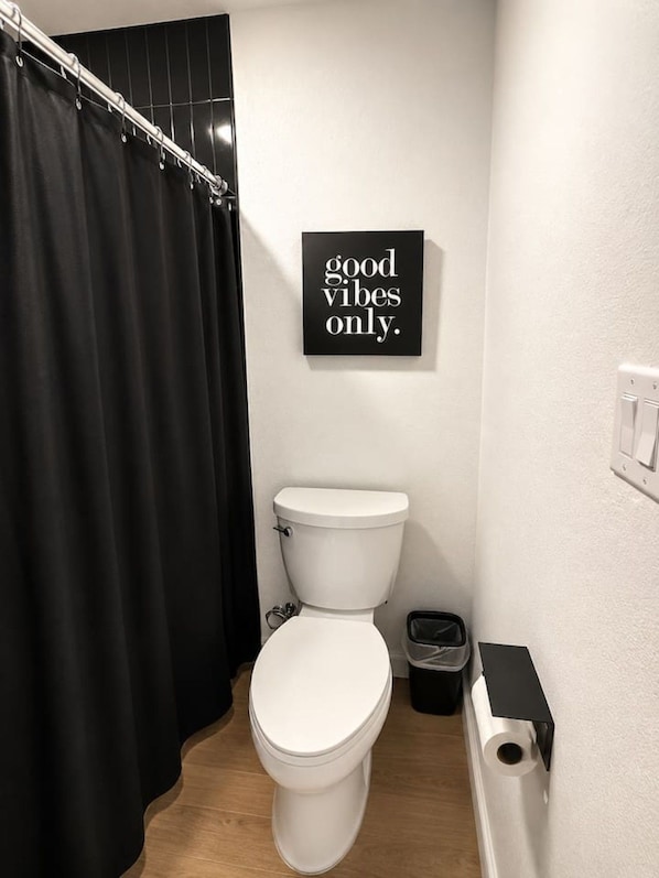 A bathroom with a white toilet, a black shower curtain, and a sign that says 'good vibes only.'