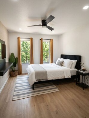 A bedroom with a bed, a ceiling fan, a TV, and a window with curtains. - Austin Hideaway | 3BR Home with Private Backyard (Austin)