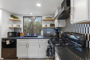 A modern kitchen with white cabinets, a black stove, and a window overlooking trees.