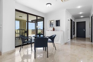 A spacious room with a dining area featuring a table and chairs, a large sliding glass door leading to an outdoor patio, and a hallway with a door. - Palm Aruba 418 | Modern Island Getaway (Palma Real)