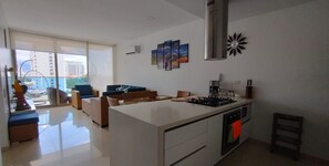 A modern kitchen with a central island, a dining area with sofas, and a large window offering a view of buildings. - New Listing (Santa Marta)