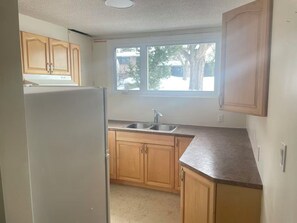 A kitchen with wooden cabinets, a refrigerator, a sink, and a window. - A quiet and private small home where you can cook and do laundry. (Ottawa)