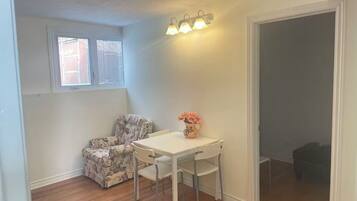 A room with a white table and chairs, a floral armchair, a vase with flowers, and a wall-mounted light fixture.