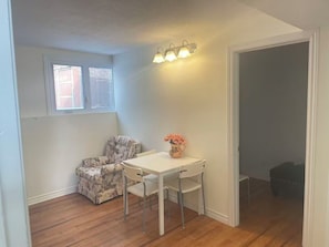 A room with a white table and chairs, a floral armchair, a vase with flowers, and a wall-mounted light fixture.