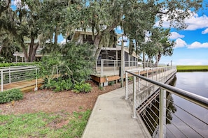A wooden deck with metal railings overlooking a body of water, surrounded by lush greenery and trees with hanging moss. - Oceanfront, pet-friendly 1-bedroom on the ground floor (Fernandina Beach)