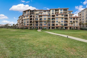 A multi-story residential building with balconies, a grassy lawn, and a clear sky. - Oceanfront, pet-friendly 1-bedroom on the ground floor (Fernandina Beach)
