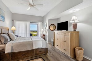 Ein Schlafzimmer mit einem Bett, einem Deckenventilator, einem Fernseher, einem Schminktisch und Blick ins Freie.