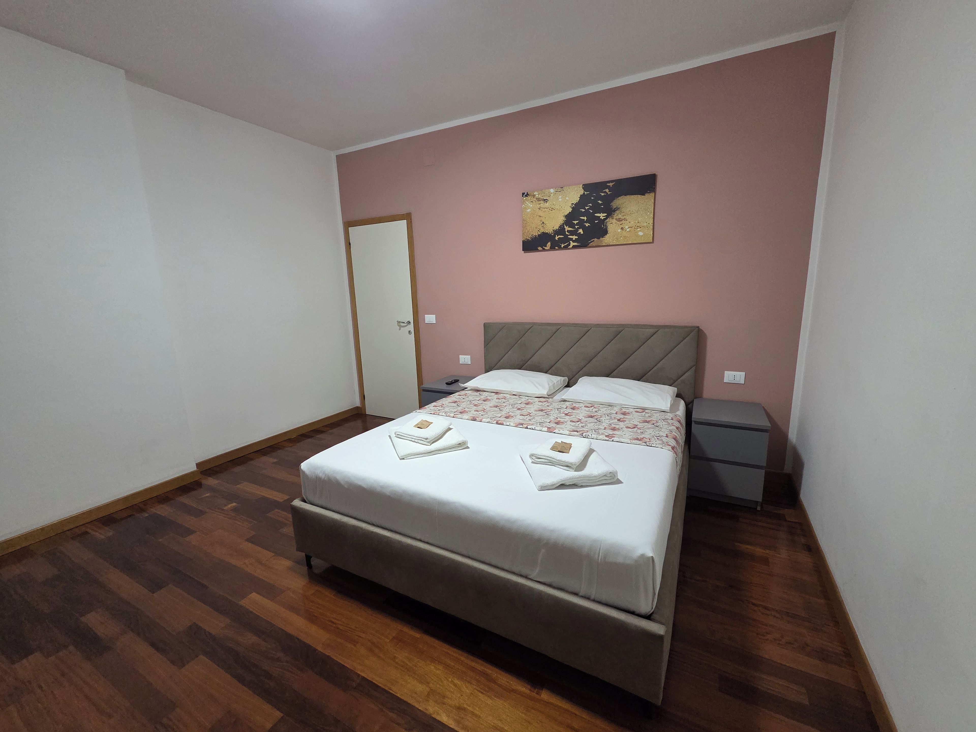 Una camera da letto con un letto, comodini, un appendiabiti a muro e un'opera d'arte appesa al muro.