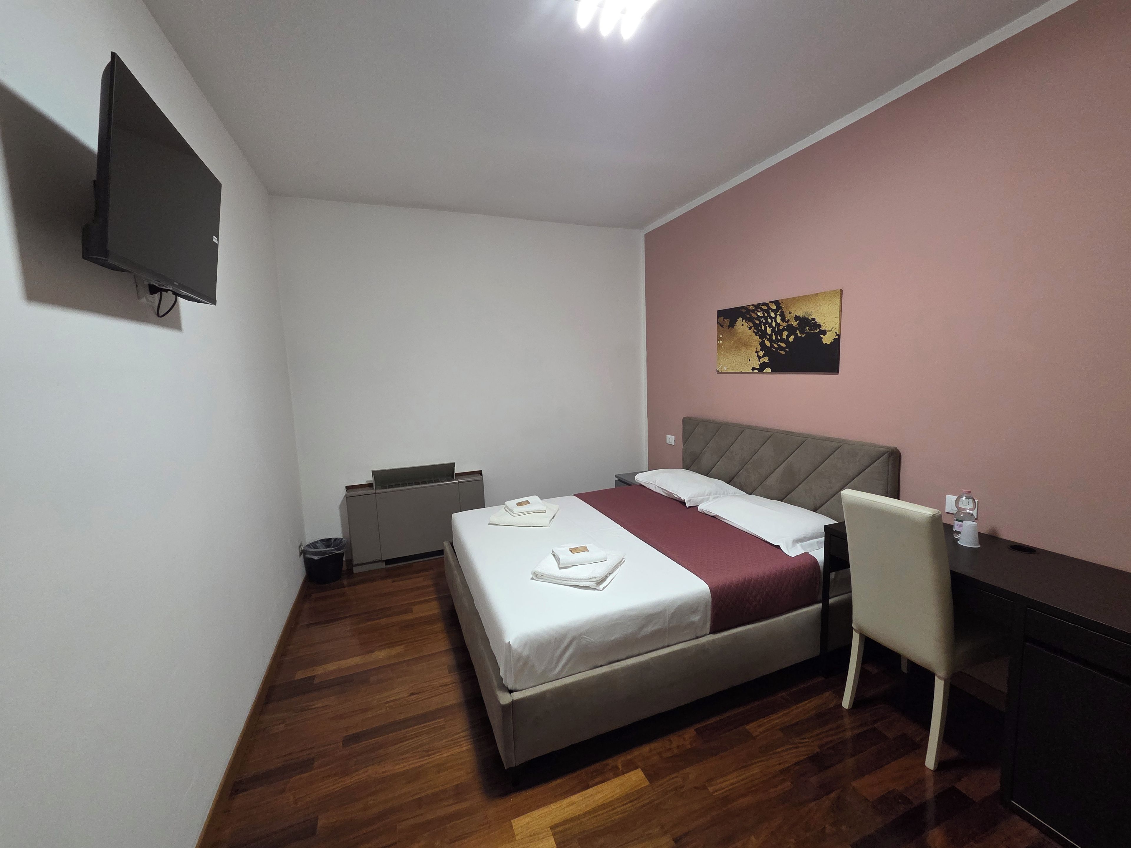 Un dormitorio con cama, escritorio, silla, televisor y cubo de basura.