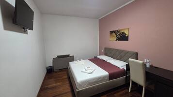 Un dormitorio con cama, escritorio, silla, televisor y cubo de basura.