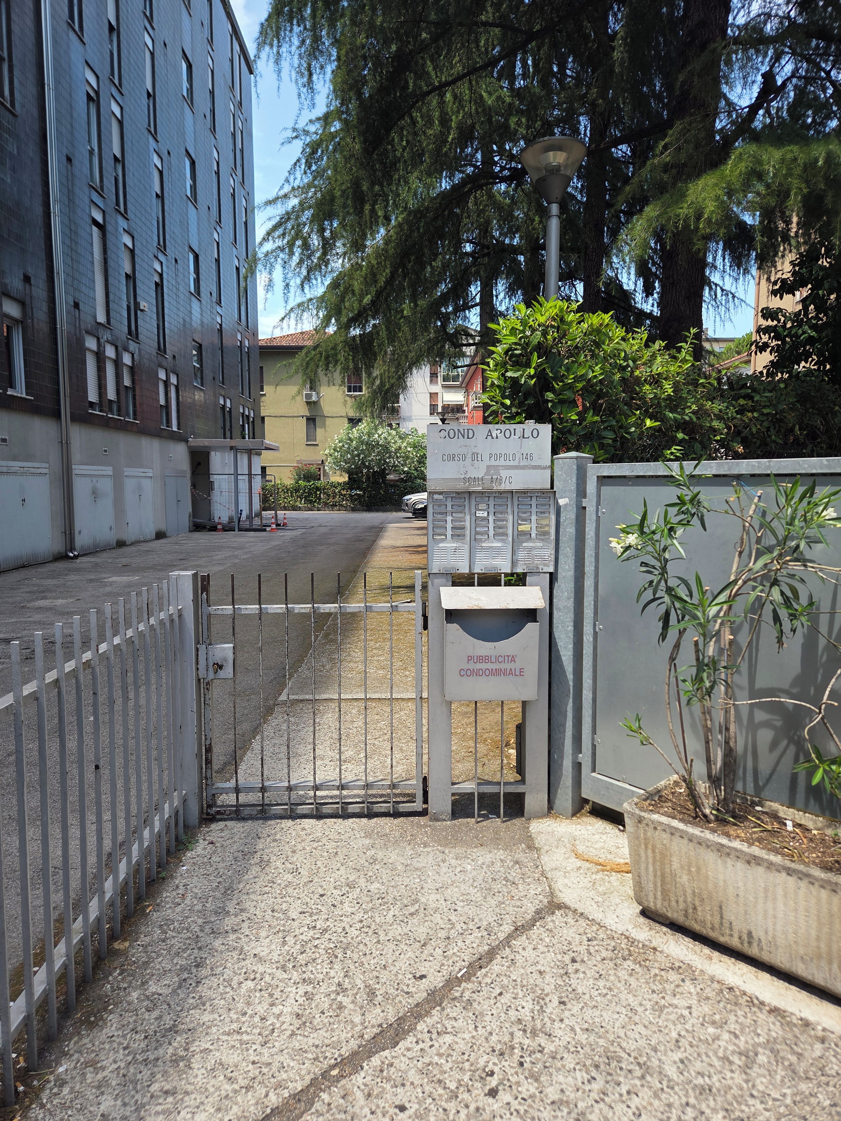 Una entrada vigilada a un área residencial con un letrero que indica 'COND. APOLLO' y 'CORSO DEL POPOLO 146'.