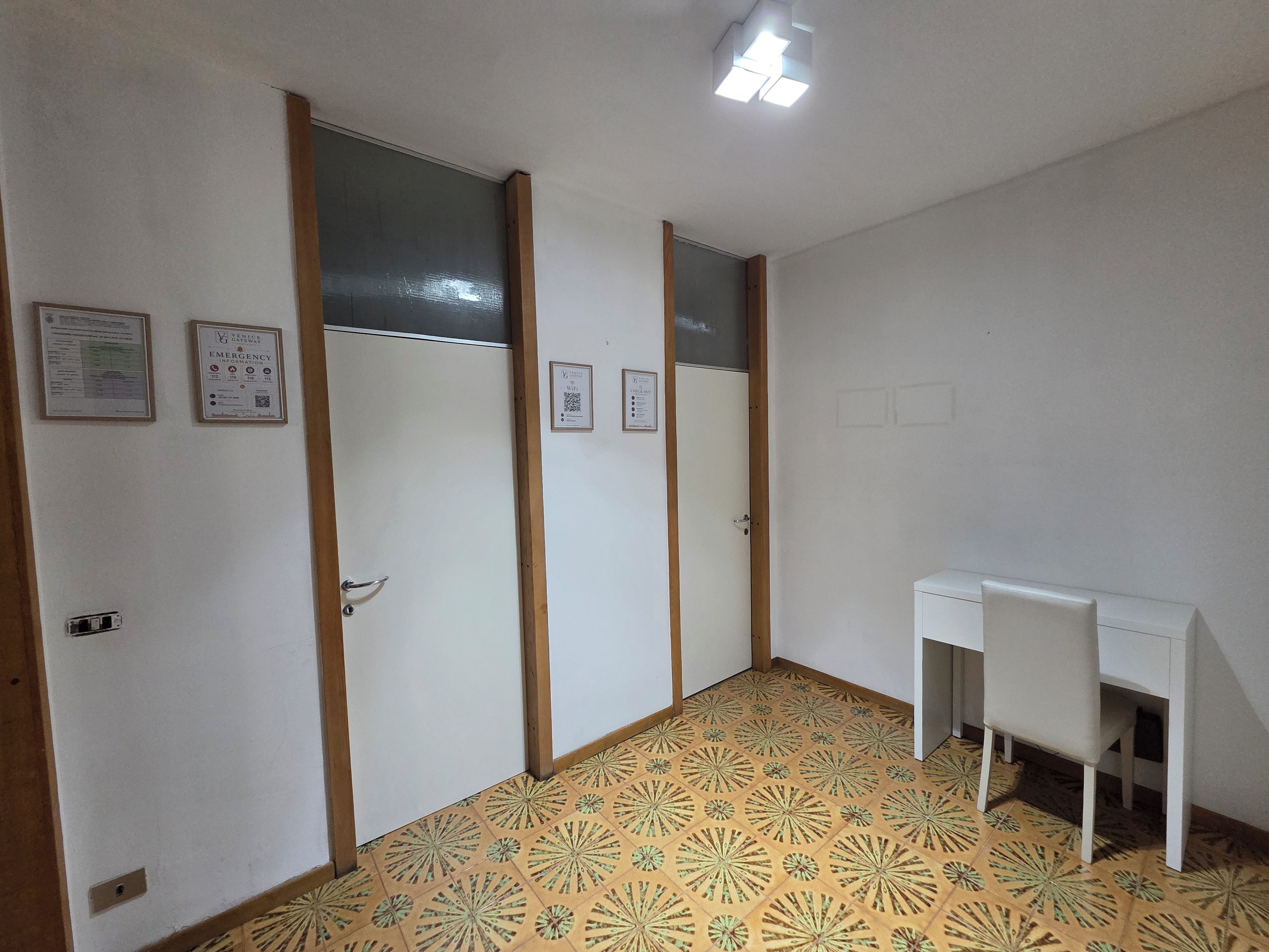 Habitación con piso estampado, un escritorio y sillas. Se observan puertas con señalización de información de emergencia.
