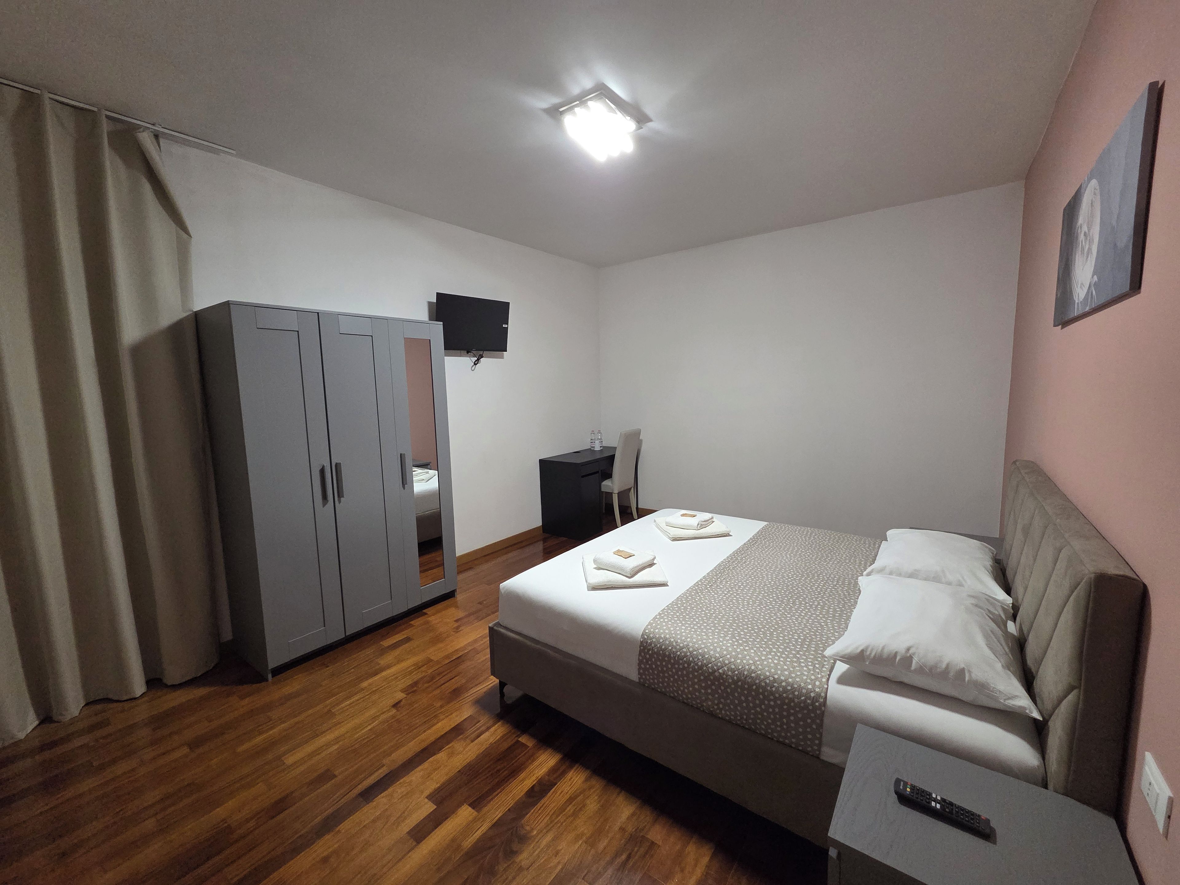 Ein Hotelzimmer mit Bett, Schreibtisch, Kleiderschrank, Flachbildfernseher und Deckenleuchte.