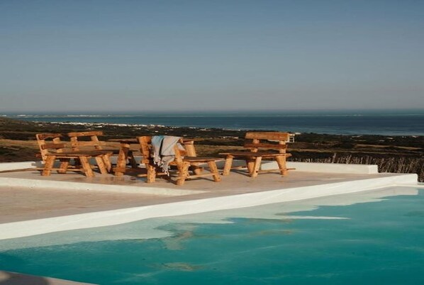 A pool with wooden benches and a view of the ocean.