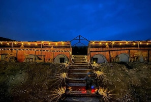 A building with a staircase leading to a central entrance, surrounded by wooden structures with string lights.