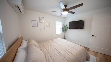 A bedroom with a bed, a ceiling fan, a mounted TV, and framed pictures on the wall.