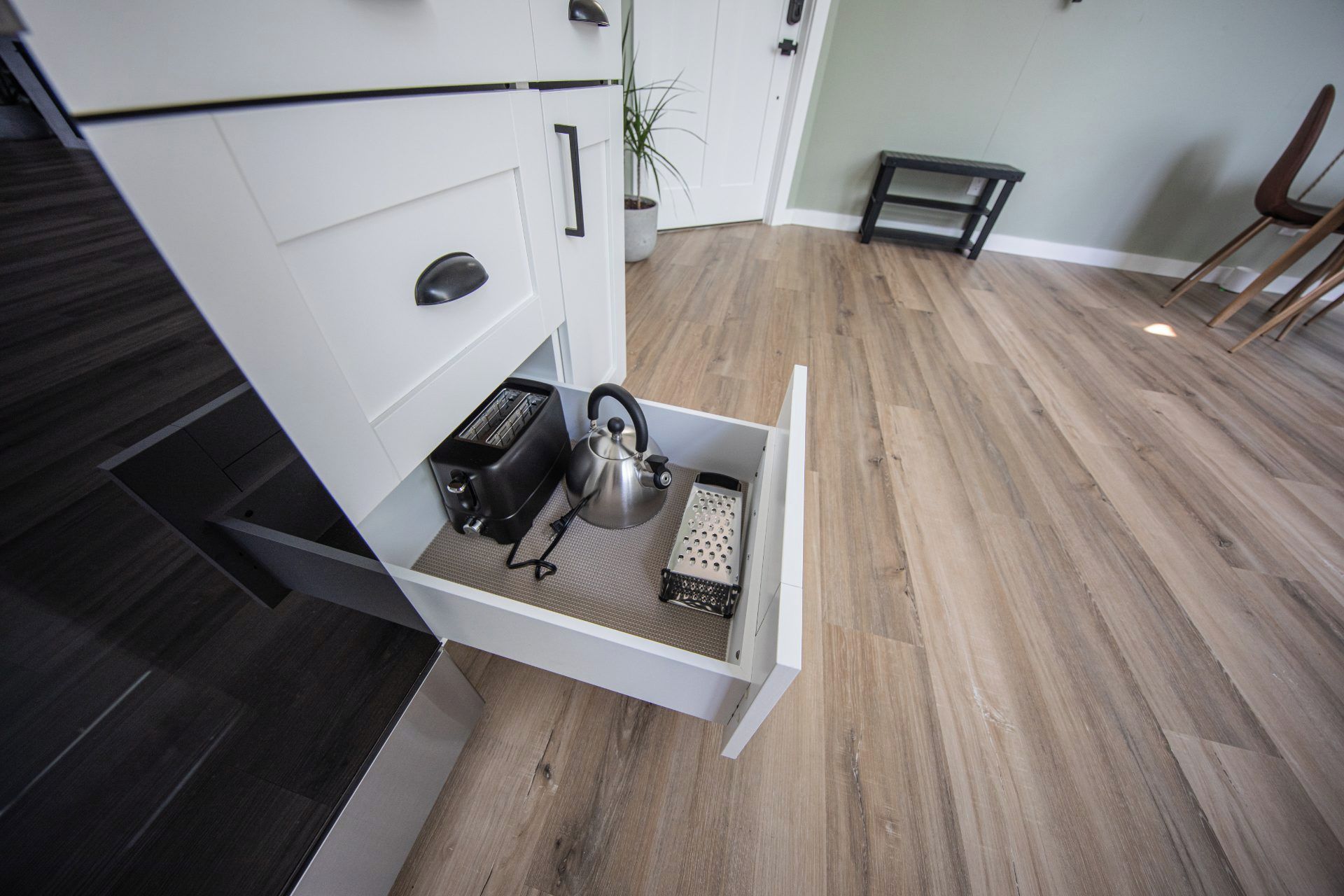 A kitchen with a built-in drawer containing a kettle, toaster, and grater.