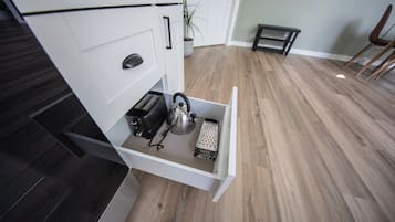 A kitchen with a built-in drawer containing a kettle, toaster, and grater.