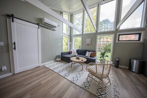 A spacious room with a large window, a sofa, a round coffee table, and a wicker chair. - Modern 3-bedroom Duplex in Bethel, EV Charging, 10 mins to Sunday river (Bethel)