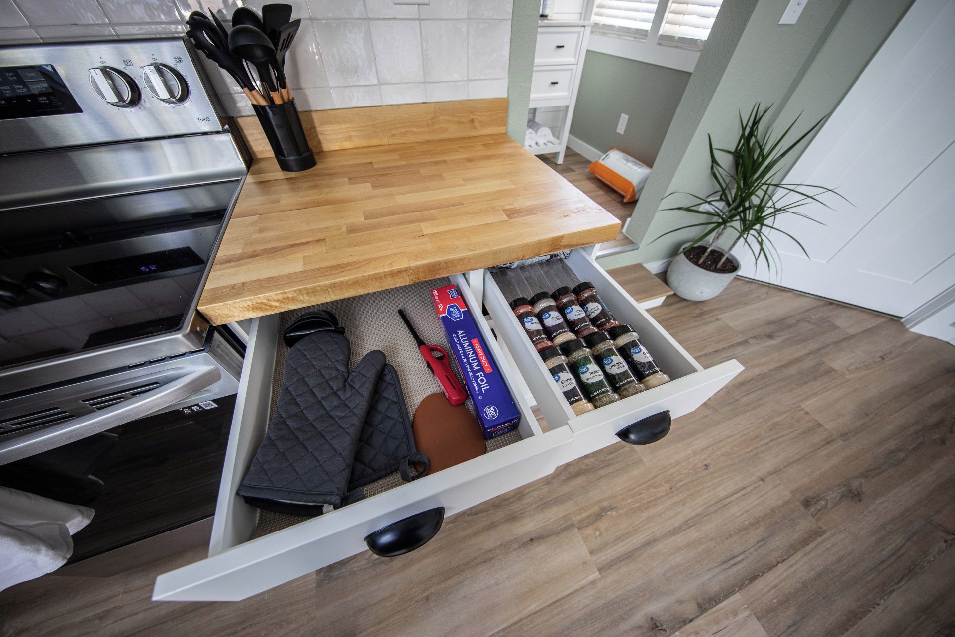Una cocina con encimera de madera, un cajón con utensilios básicos y una planta en maceta.