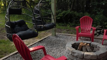 A patio with red chairs, a hanging chair, and a stone fire pit.
