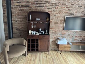 A room with a brick wall, a wooden cabinet with shelves, a television, a sofa, and a small table. - Room 206, Ilium Luxury Hotel Downtown Troy (Troy)