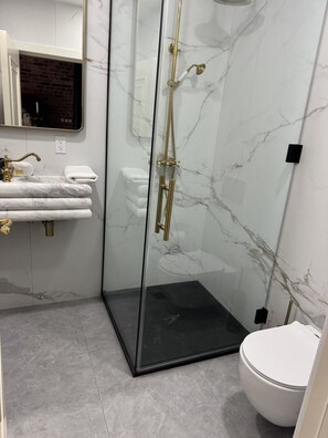 A modern bathroom with a glass-enclosed shower, a white toilet, and a marble-tiled wall. - Room 206, Ilium Luxury Hotel Downtown Troy (Troy)