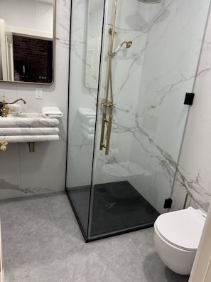 Ein modernes Badezimmer mit einer gläsernen Duschkabine, einer weißen Toilette und einer Wand mit Marmorplatten.