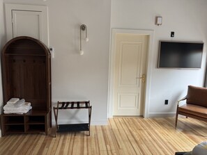 A room with a wooden wardrobe, a bench, a door, and a television mounted on the wall. - Room 204, Ilium Luxury Hotel Downtown Troy (Troy)