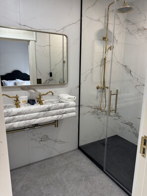 A bathroom with a marble wall, a glass-enclosed shower, a gold faucet, and a mirror. - Room 204, Ilium Luxury Hotel Downtown Troy (Troy)