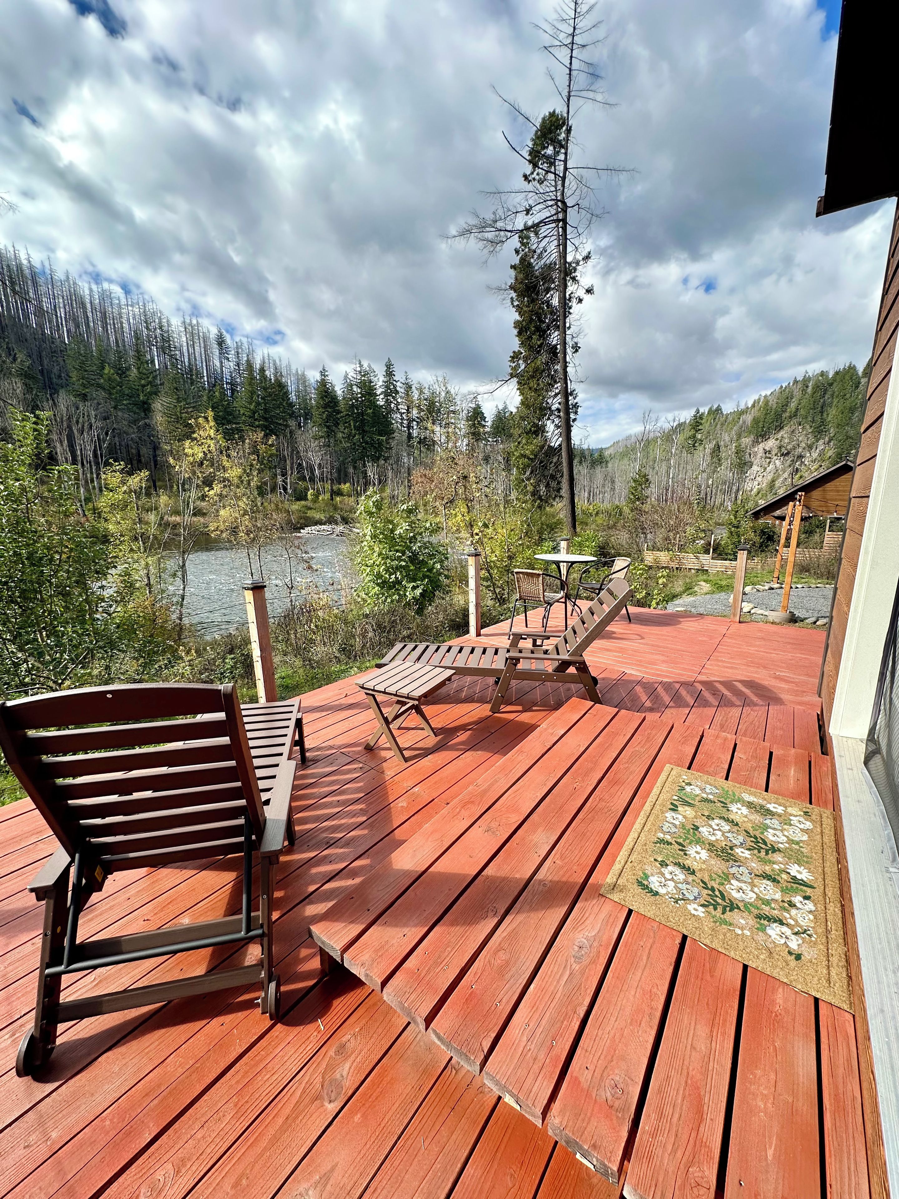 A wooden deck with a bench and table, overlooking a forested area and a body of water.
