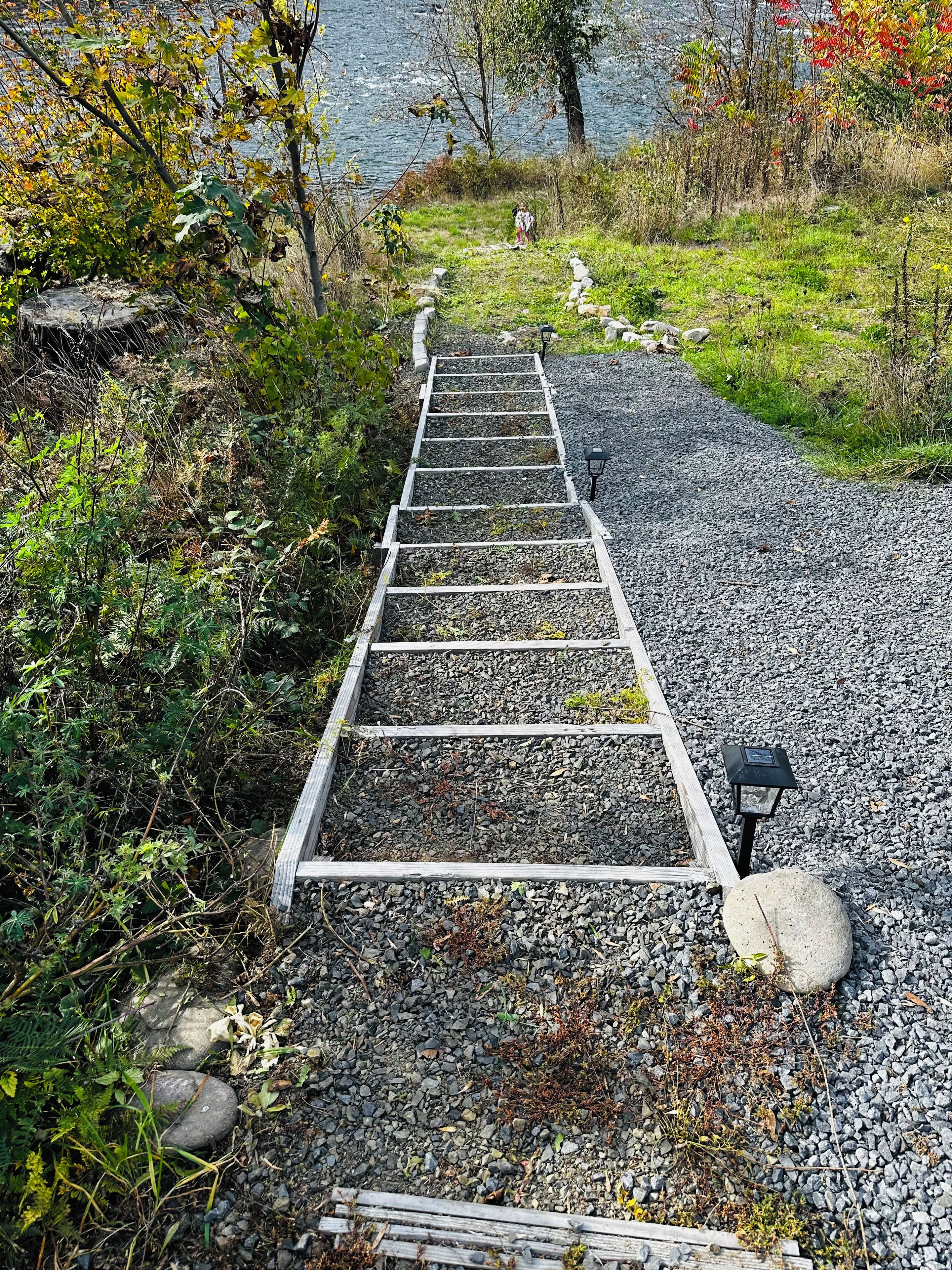 Un sentier en bois qui mène à un plan d’eau, entouré de végétation et de rochers.