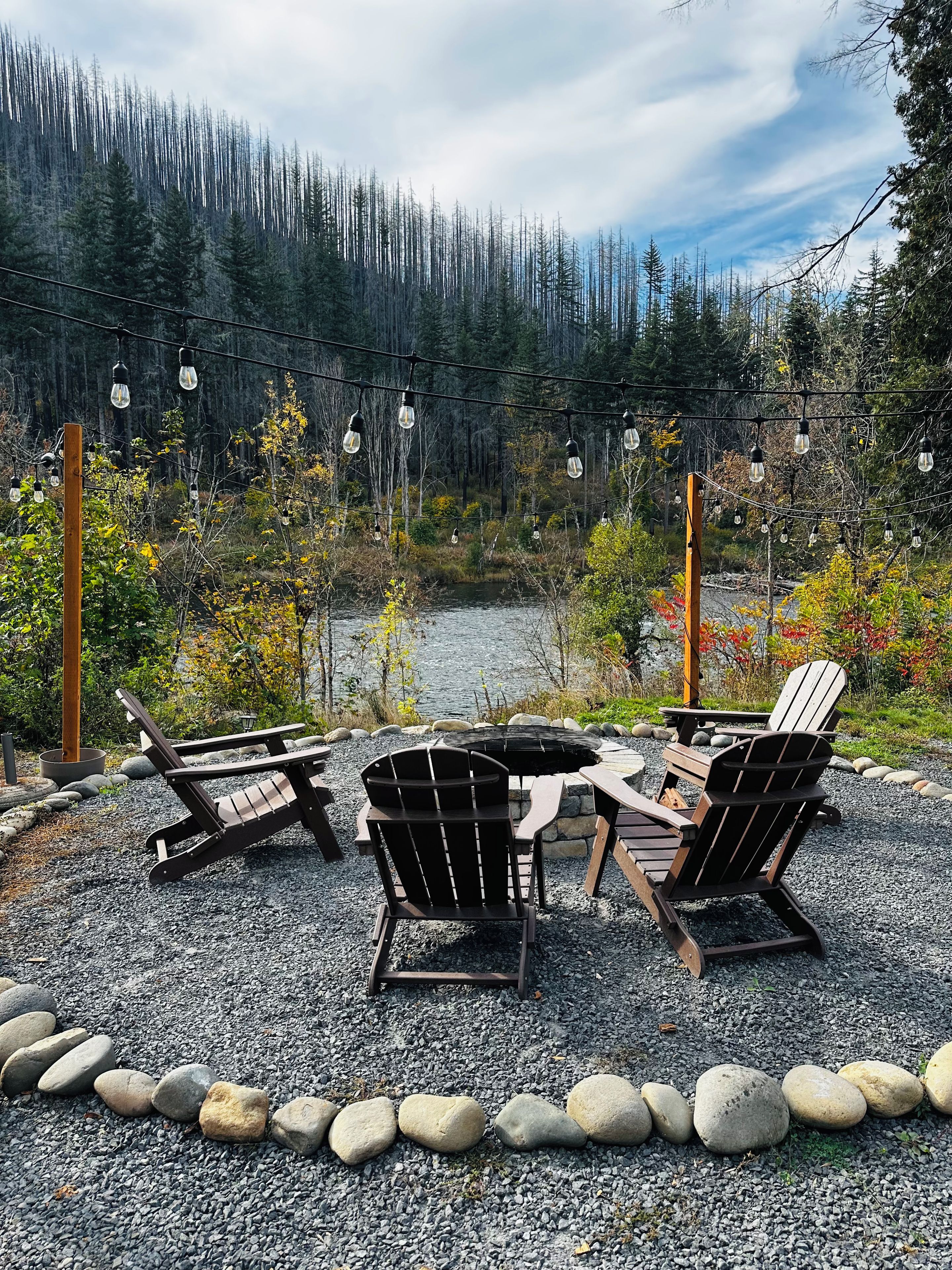 An outdoor seating area with Adirondack chairs and a table, surrounded by a gravel path and a wooden border.