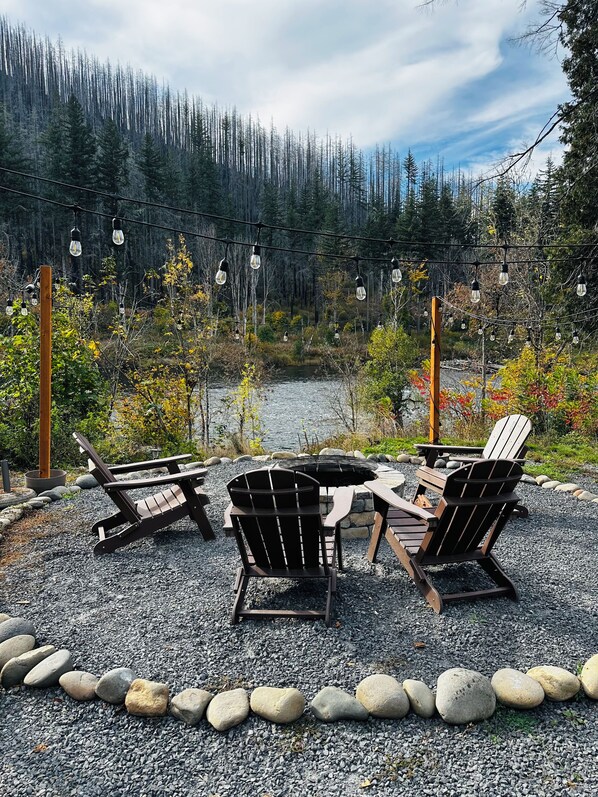 An outdoor seating area with Adirondack chairs and a table, surrounded by a gravel path and a wooden border.