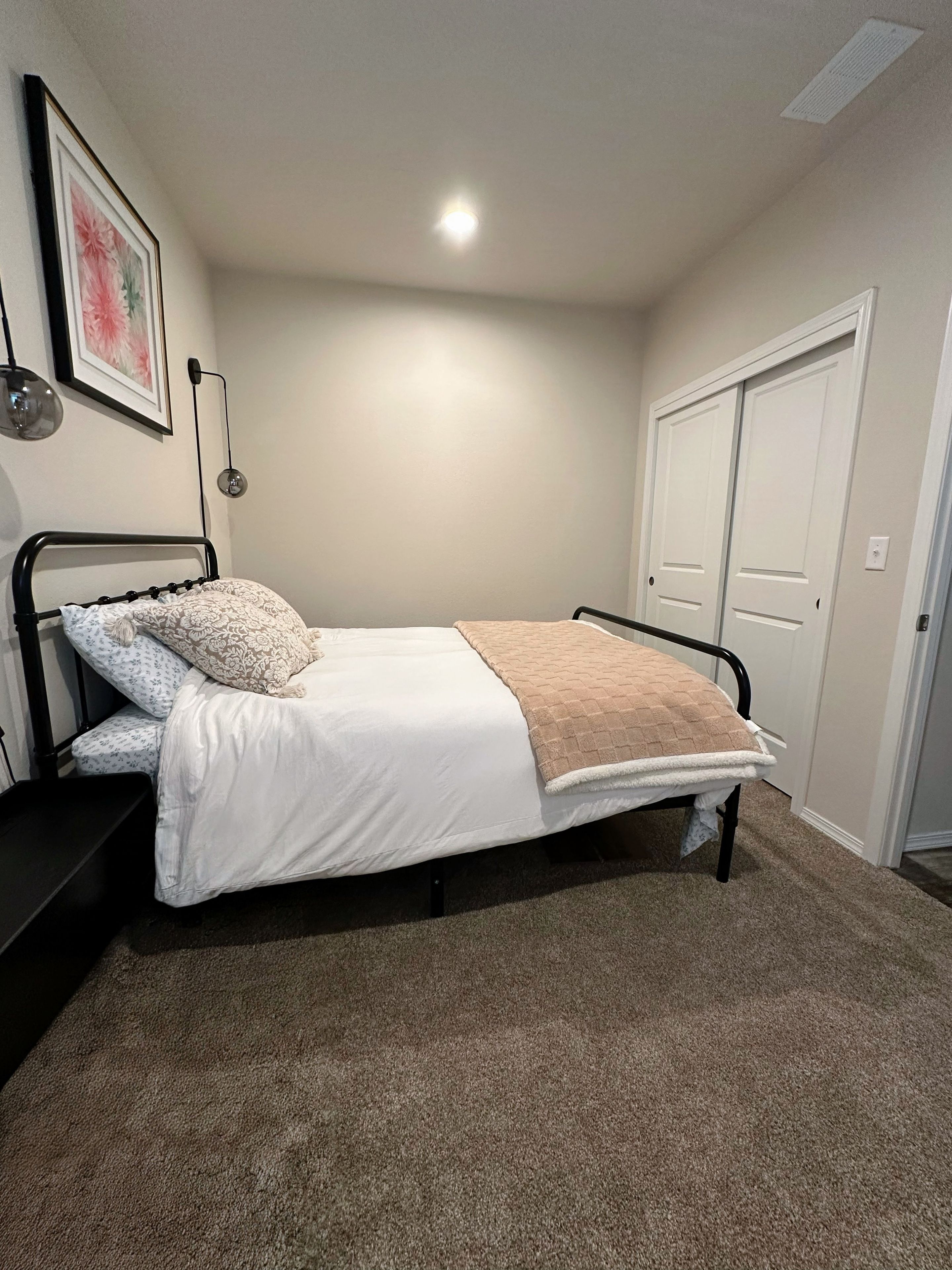 A bedroom with a bed, a wall-mounted light, a door, and a carpeted floor.