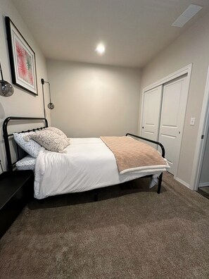 A bedroom with a bed, a wall-mounted light, a door, and a carpeted floor. - Comfy Flat with RiverView (Vida)