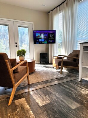 A living room with two brown chairs, a small table, a flat-screen TV mounted on the wall, and a fireplace.