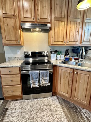 A kitchen with wooden cabinets, a stainless steel stove, a sink, and a patterned rug. - Comfy Flat with RiverView (Vida)