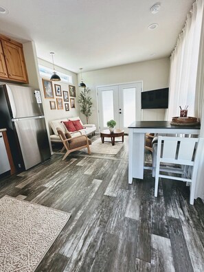 A modern kitchen with a built-in refrigerator, a dining table with chairs, a sofa with cushions, and a potted plant. - Comfy Flat with RiverView (Vida)