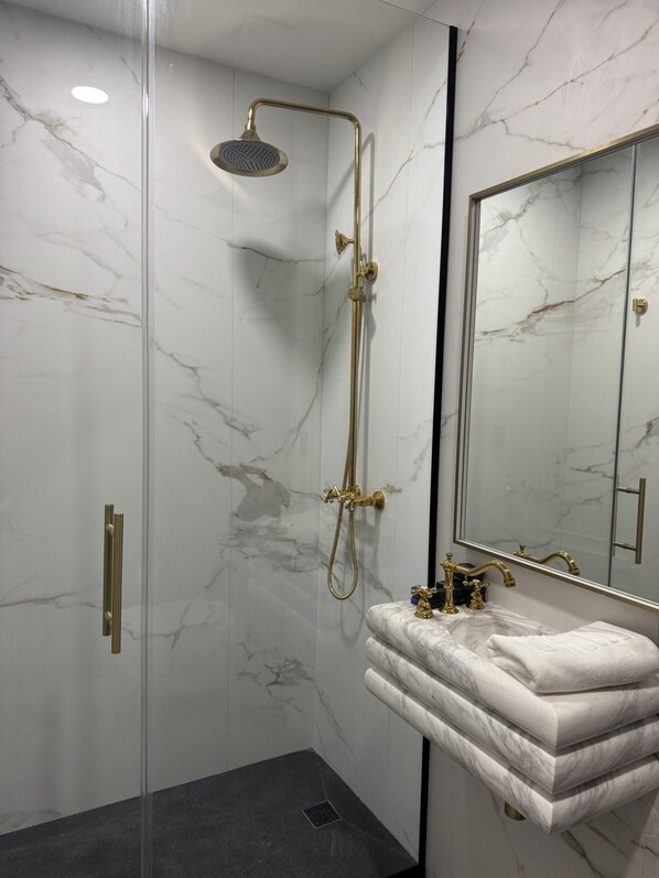 Une salle de bain avec une douche à parois de verre, un mur en marbre, un lavabo avec un robinet doré et un grand miroir.