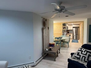 A living room with a ceiling fan, a dining area with a table and chairs, and a kitchen with a refrigerator. - Renovated Vermont Apartment | Near Stowe & Smugglers' Notch (Cambridge)