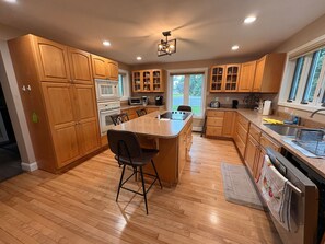 A modern kitchen with wooden cabinets, a central island, and a large window. - 3BR lakefront dog friendly home w/ views and kayaks (Colchester)