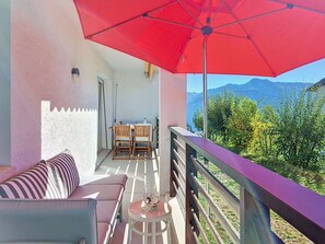 Ein Balkon mit rotem Sonnenschirm, einer Couch, einem Tisch und Stühlen.