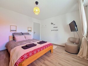 Ein Schlafzimmer mit einem Bett, einem Nachttisch, einem Sessel, einem Fernseher und einer Wand mit einer Beschriftung.