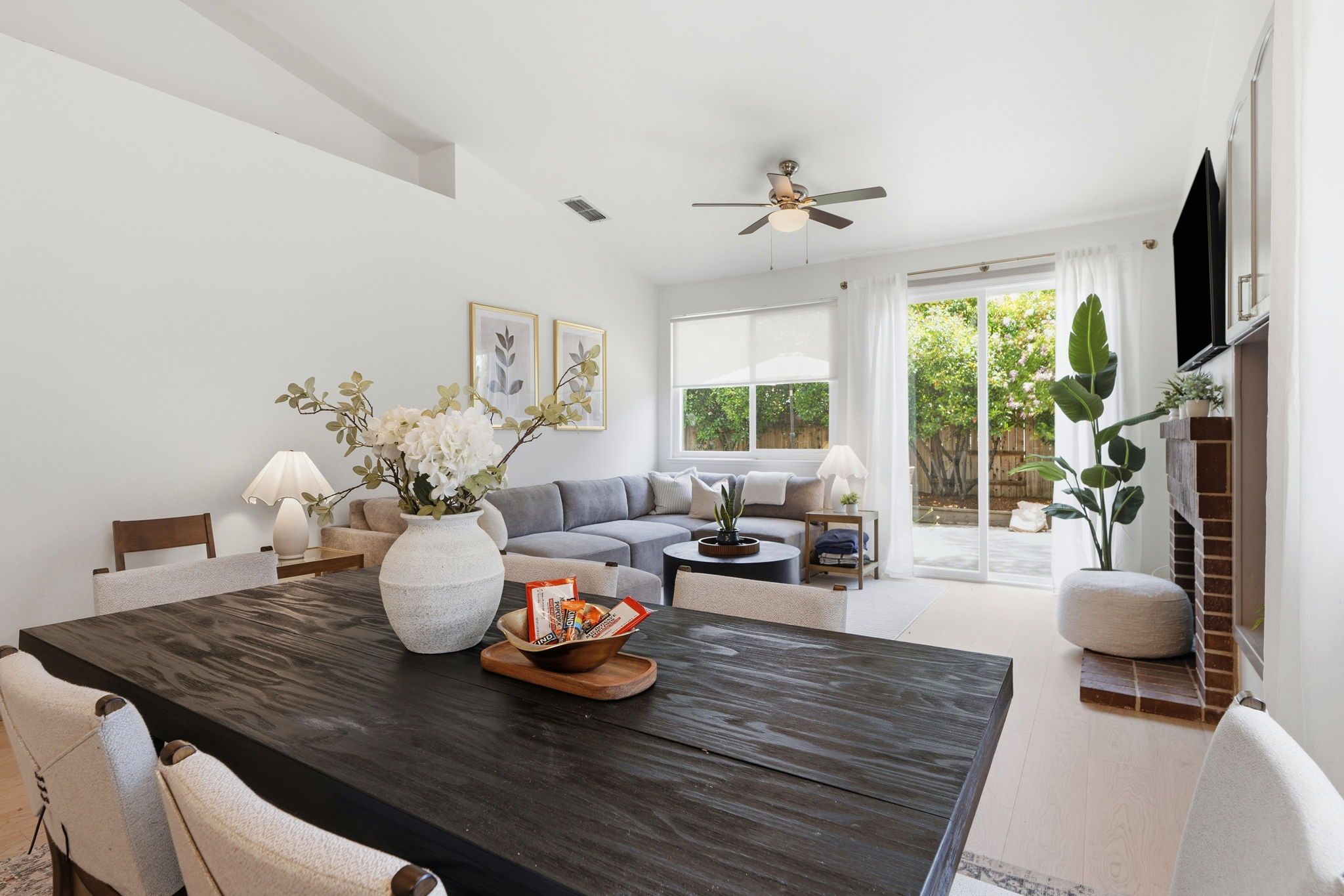 A modern living room with a dark wooden dining table, grey sofa, and a ceiling fan.