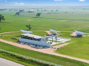 A modern hotel with a pool area, surrounded by expansive green fields and a clear sky. - Blue Skies Retro Resort | Private Pool & Shastas (Fredericksburg)