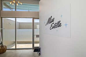 A modern interior with a sliding glass door leading to a balcony, a wall-mounted sign reading 'Miss Estrella', and a wicker basket on the floor. - Blue Skies Resort | Glamping | Pool | Fireplace (Fredericksburg)